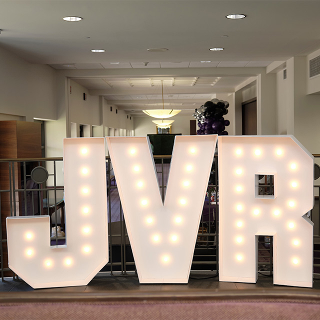 Illuminated block letters spelling "JVR" surrounded by festive balloons.