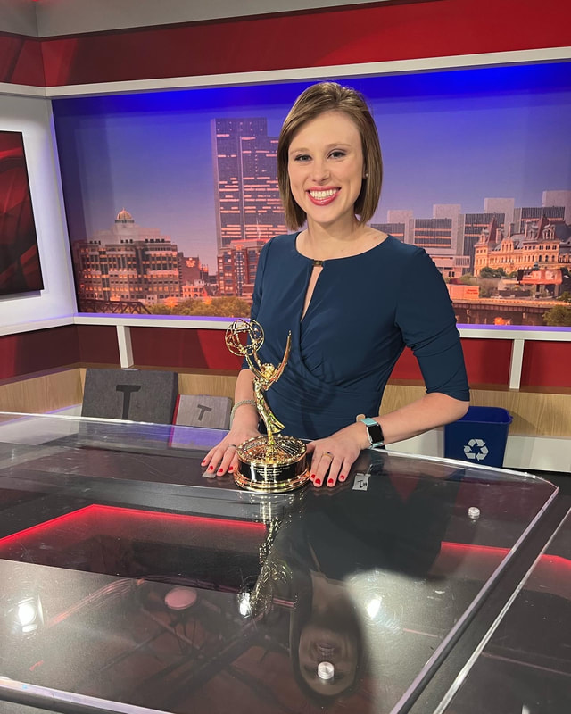Rachel Tiede smiling at a news desk with her Emmy award in hand