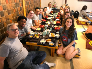 Dr. Michael Strausz and Dr. Wendy Williams sit on the floor, gathered around a low table for a traditional Japanese meal with their Honors students