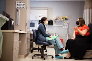 Courtney Sullivan, seated on an office chair and holding a folder, consults with a patient