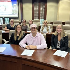 Students seated, smiling, along one side of the Debate Chamber