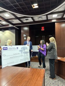 Three students present a large display check to one of their charity recipients