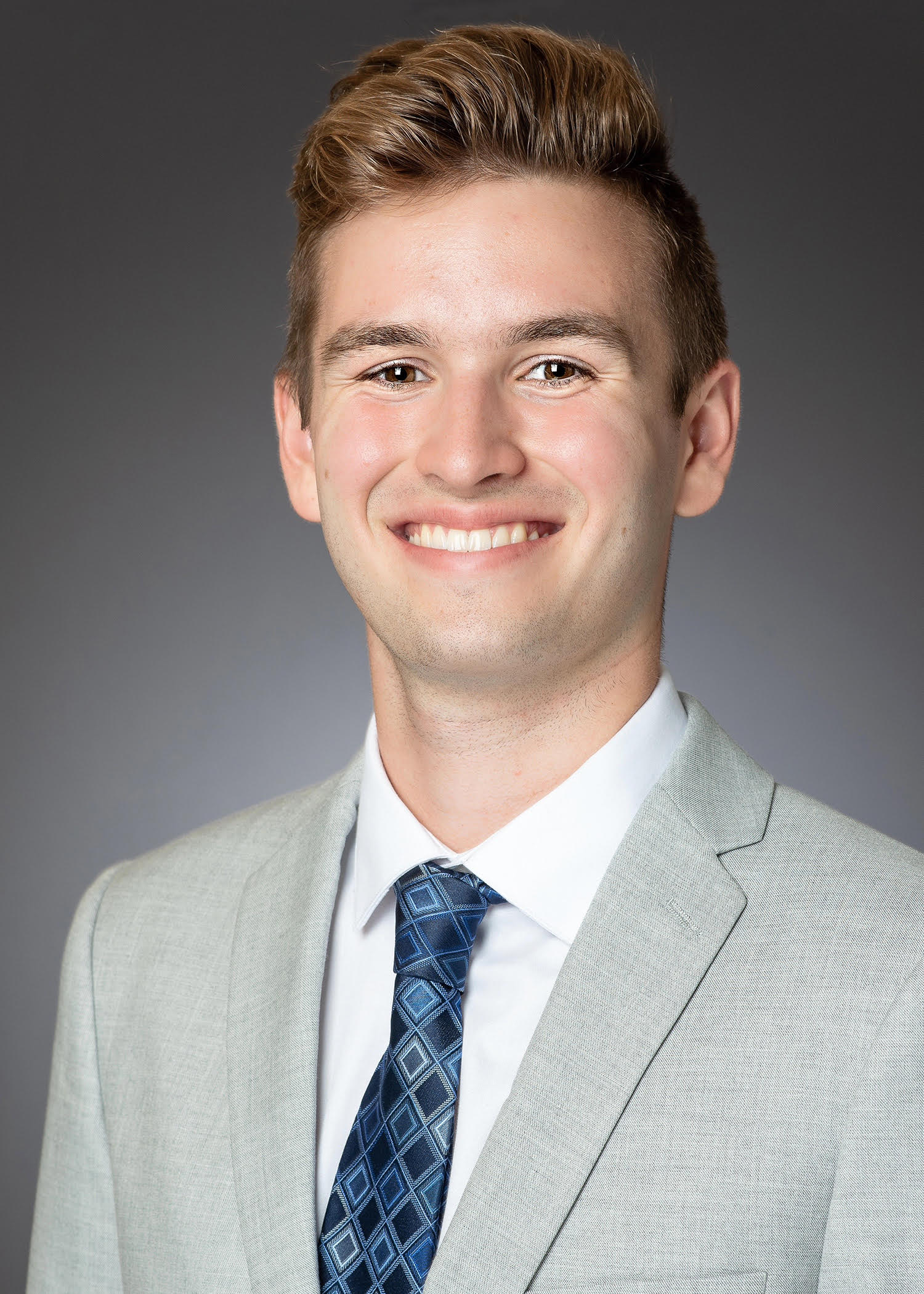 Ethan Gray smiling in headshot photo wearing grey suit and necktie.