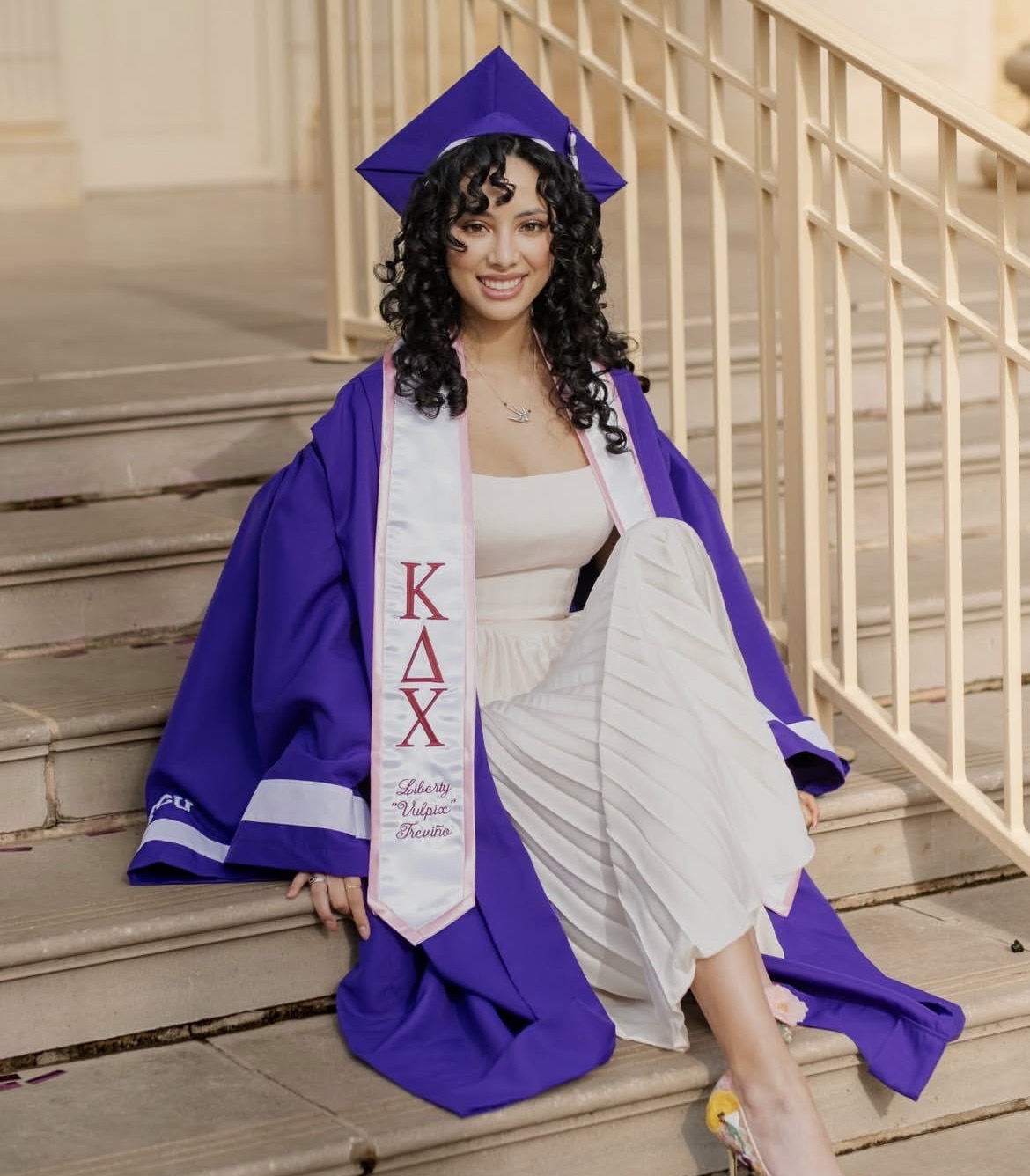 Liberty Trevino sitting on steps wearing purple graduation cap and gown